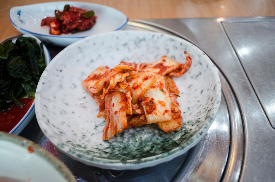 Close-up of spicy Korean kimchi served in a traditional ceramic bowl on a dining table.