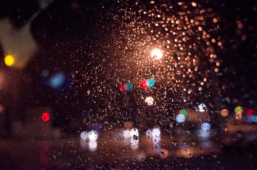 Artistic view of raindrops on a window with blurred city lights in the background creating a moody night scene.