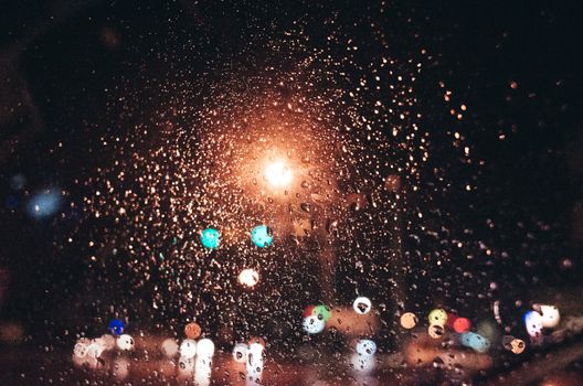 Close-up of raindrops on a window with blurred city lights in the background, captured at night.