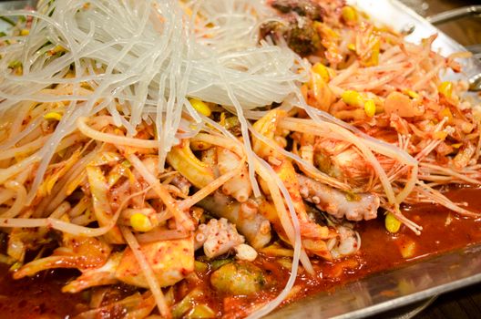 Close-up of a vibrant Korean seafood and noodle dish with kimchi.