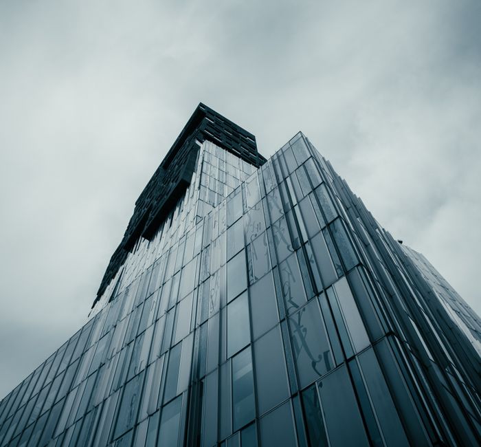 Low angle view of a modern glass skyscraper under a cloudy sky, showcasing contemporary architecture.