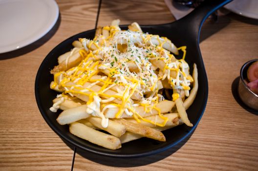 Mouthwatering french fries topped with cheese and herbs, served in a stylish black pan on a wooden table.