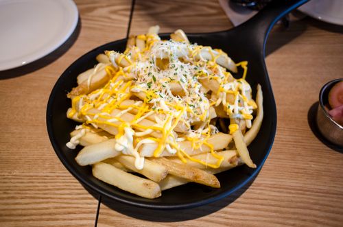 Free Mouthwatering french fries topped with cheese and herbs, served in a stylish black pan on a wooden table. Stock Photo