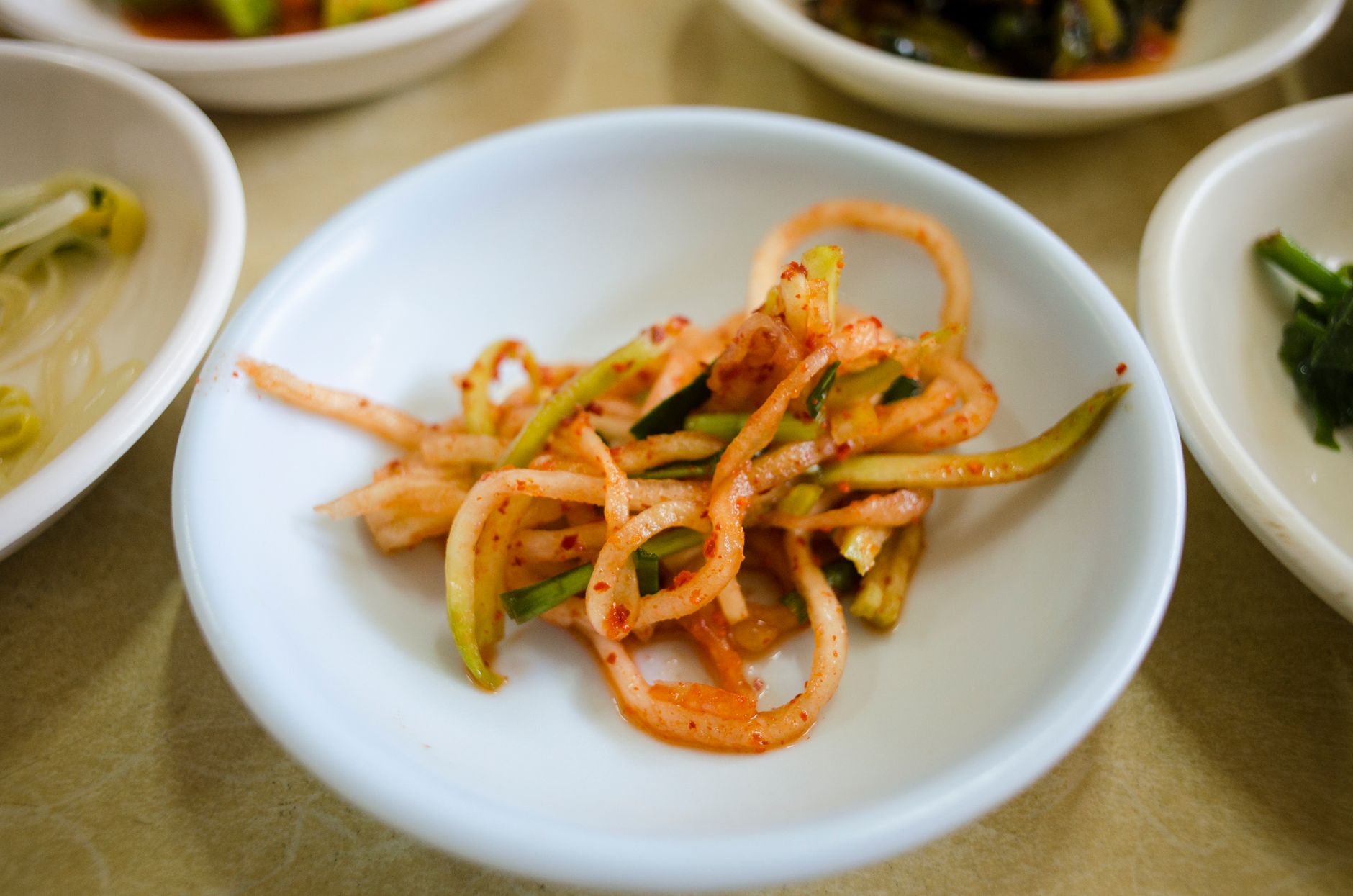 Close-up of traditional Korean banchan side dishes, highlighting spicy vegetables.