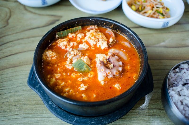Korean tofu soup in black stone bowl with side dishes