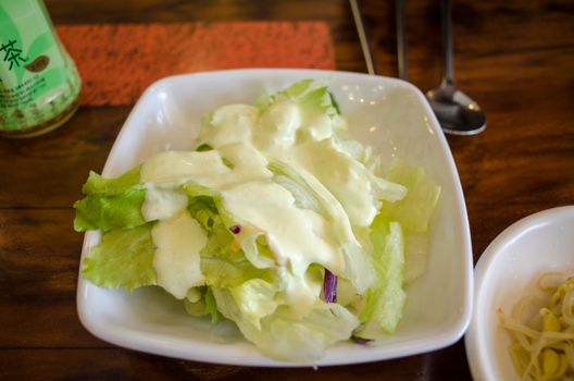Close-up of a green salad with creamy dressing in a white bowl on a wooden table.