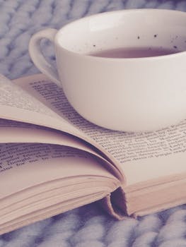 A warm and cozy scene of a book and a cup of tea on a soft knitted blanket.