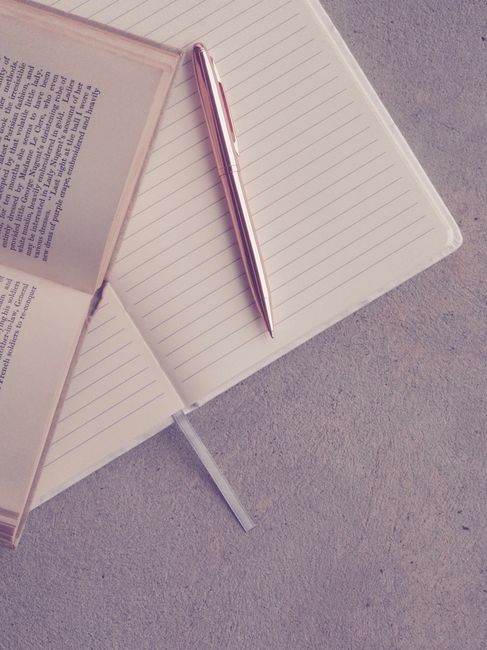 Miljöbild – Creative flatlay featuring an open book, notebook, and pen on a textured surface.