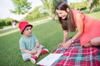 Woman in Red Cap and Gray Tank Top Sitting on Green Grass Field While Holding a during
