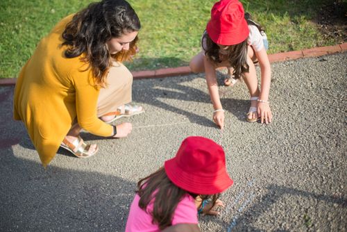 Free A nanny and two children drawing together on the pavement outdoors in Portugal. Stock Photo
