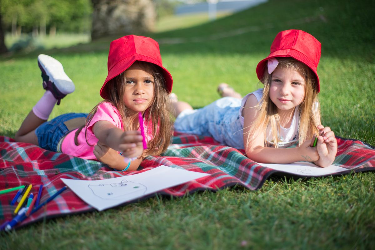 Two girls drawing on a picnic blanket at camp
