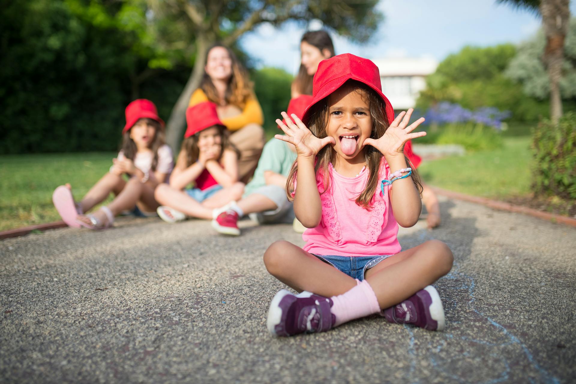 Group of children wearing red hats having fun outside, showing playful gestures and smiles.