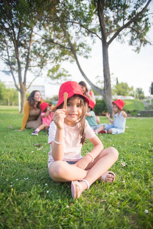 A Young Girl Wearing a Red Hat Sitting on the Grass