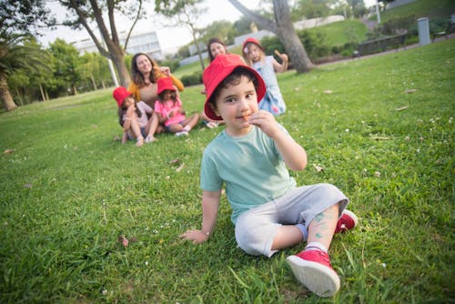 Close-Up Shot of a Boy with Red Hat Sitting on Grass