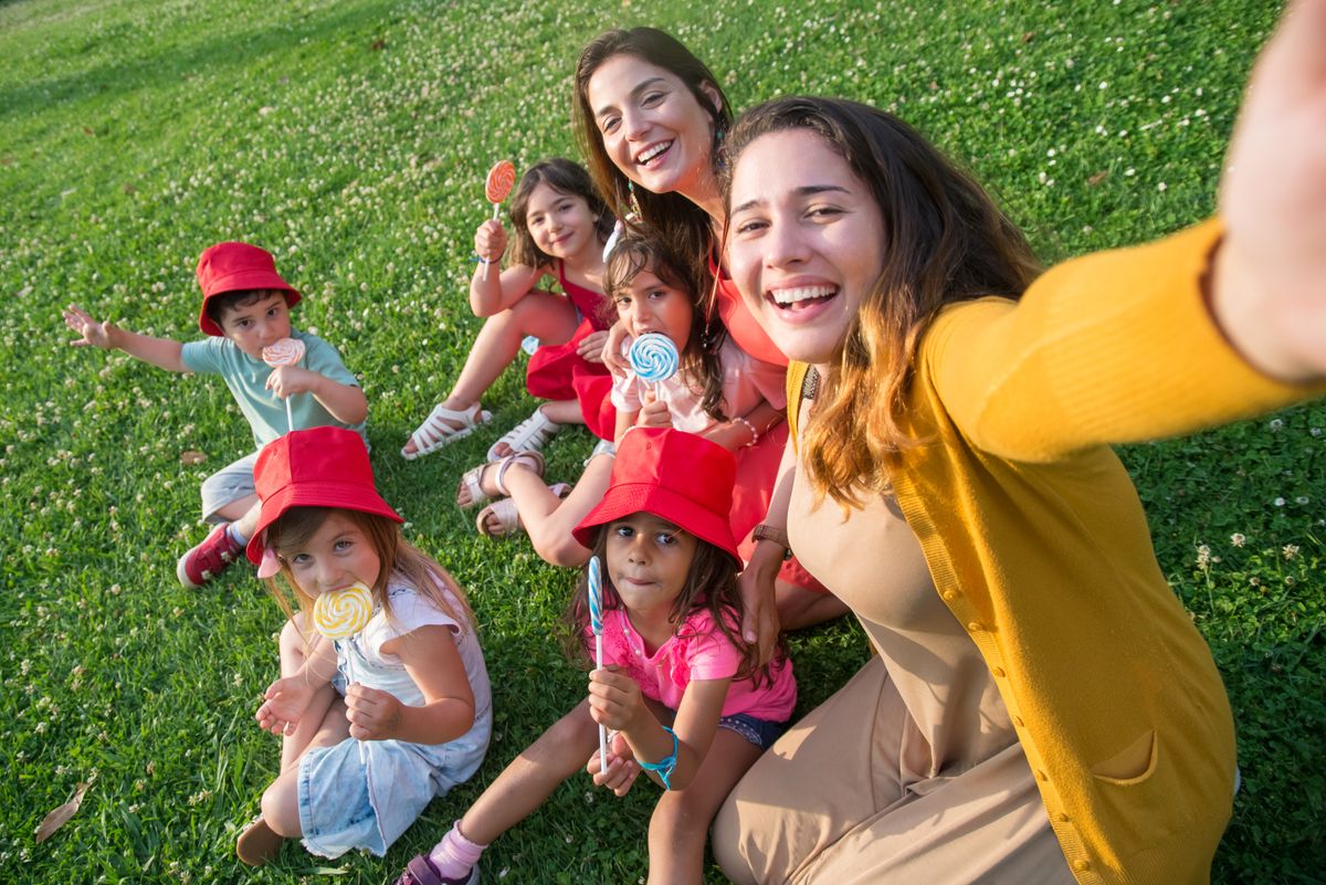 Joyful gathering of women and children on a sunny day, capturing a group selfie outdoors while enjoying lollipops.