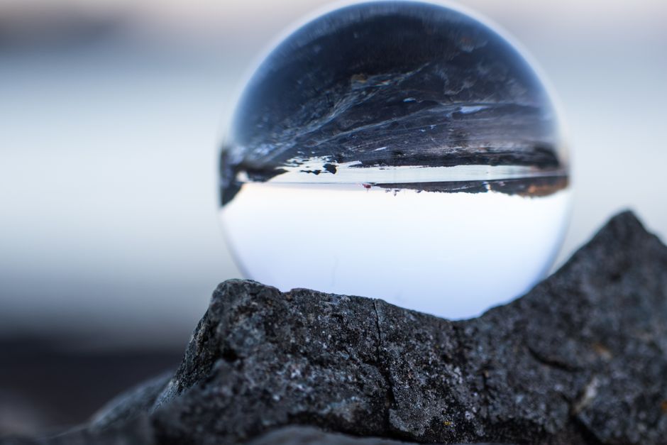 Close-up of a crystal ball reflecting a serene landscape on a rocky surface.
