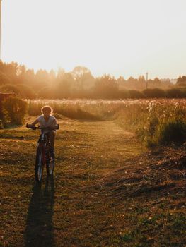 A child rides a bicycle down a sunlit path through a picturesque meadow at sunset.