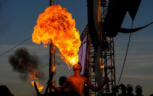 Shirtless Man Blowing Fire in a Performance
