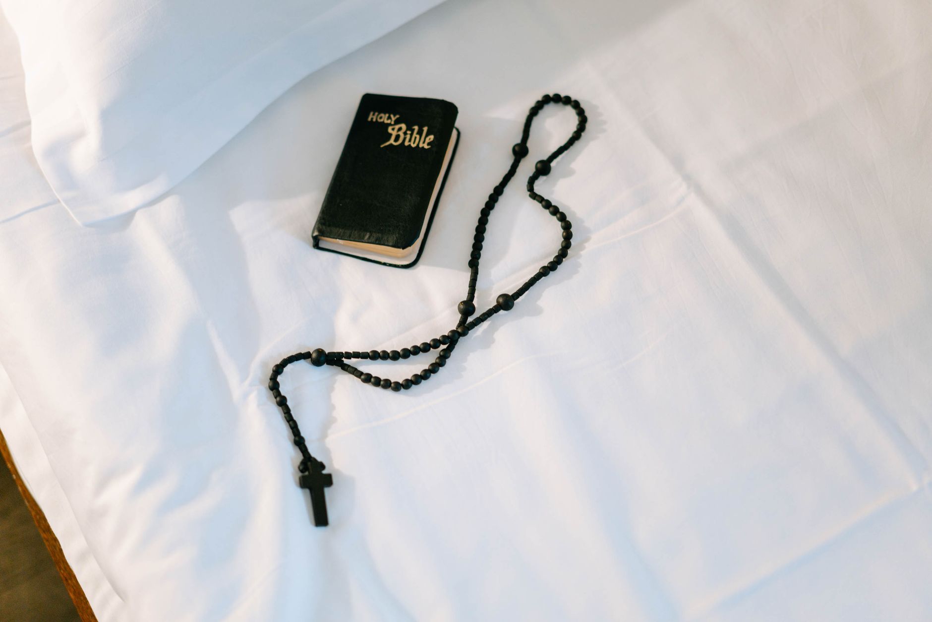 A top-down view of a Holy Bible and rosary on a white cloth, symbolizing faith and devotion.