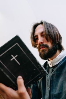 An adult man with long hair and beard reading a Bible indoors, emphasizing faith and spirituality.