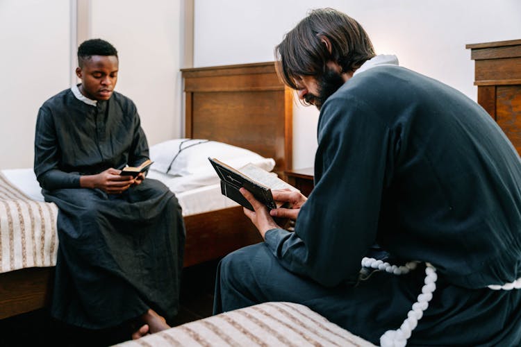 Men In Black Robes Sitting On Bedside Reading The Holy Bible