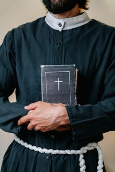 A priest in a cassock holds a holy bible close, symbolizing faith and devotion.