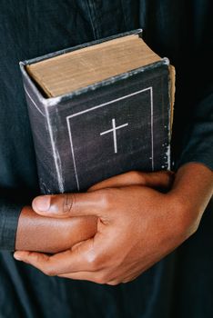 Close-up of hands holding a worn Bible featuring a cross symbol, symbolizing faith and spirituality.