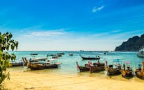 充满活力的长尾船停靠在泰国阳光明媚的海滩上，天空晴朗