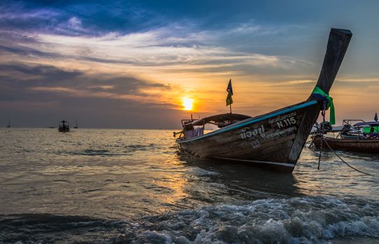 Beautiful sunset at a Thai beach with traditional fishing boats on the calm sea.