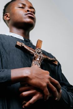 A man in a black cassock praying with a crucifix in a spiritual setting.