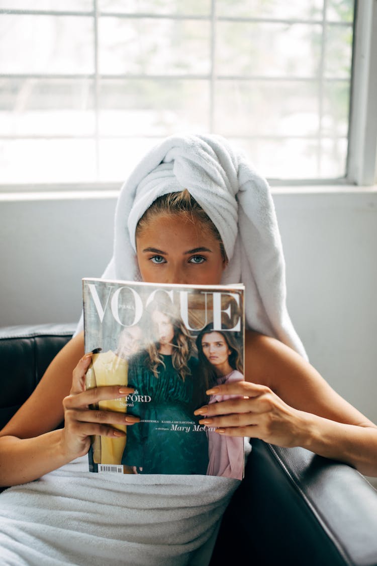 A Woman With White Towel On Hair Holding A Vogue Magazine