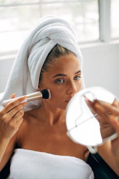Caucasian woman using a makeup brush in front of a mirror after a bath.