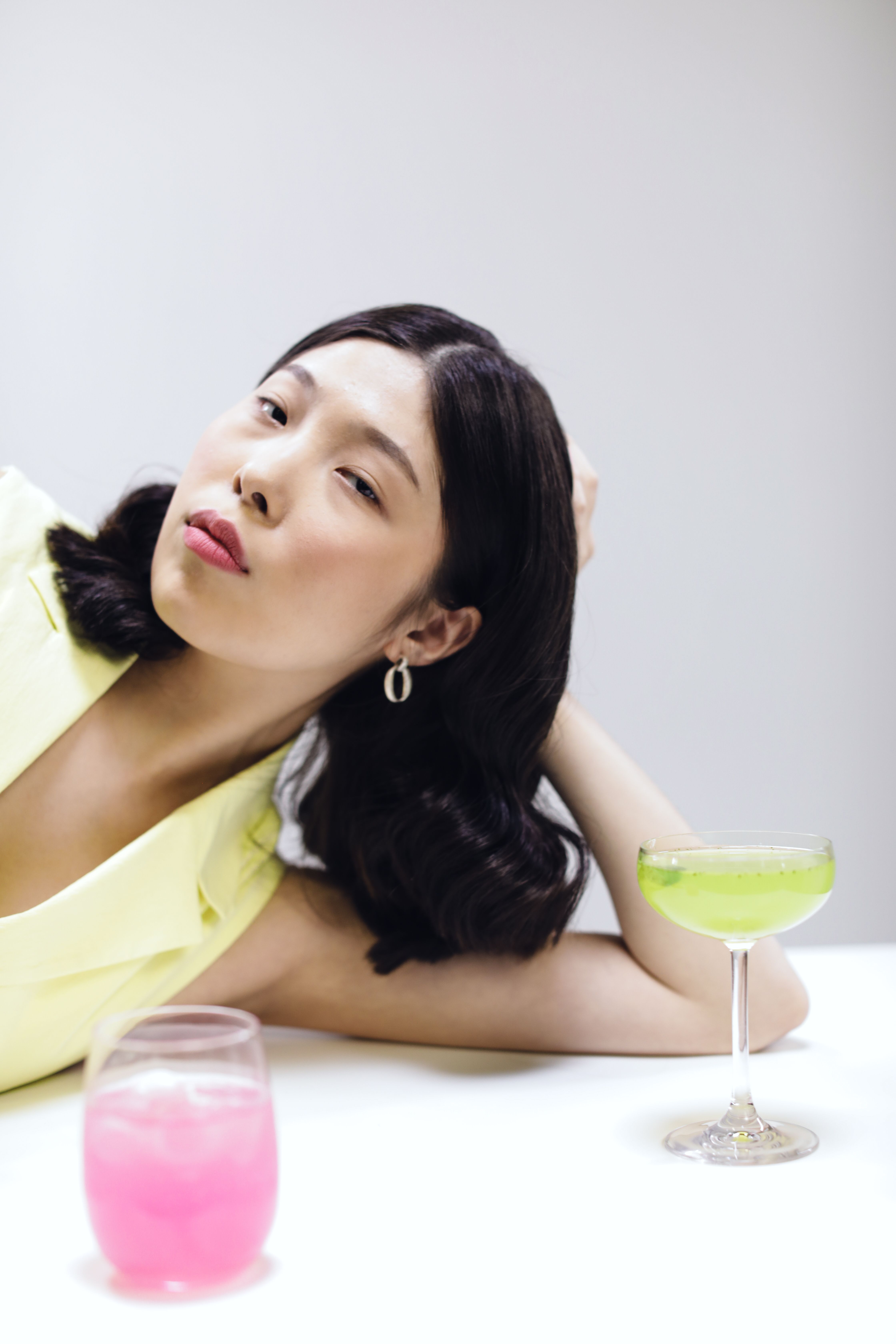Elegant Asian woman with cocktails in a minimalist studio setting.
