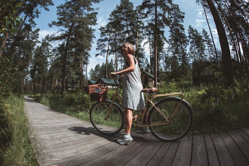 Woman in Dress Riding a Bicycle on a Wooden Pathway