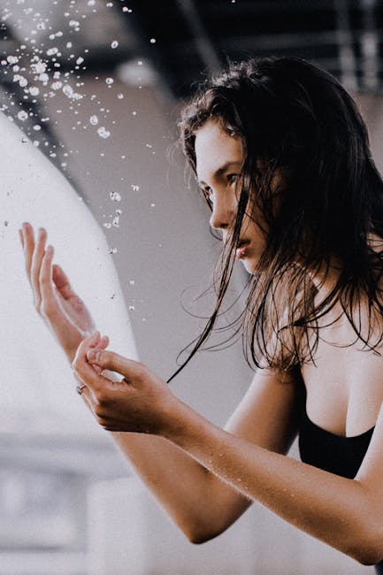 Portrait of a wet-haired Caucasian woman contemplatively engaged with water droplets.