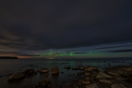 Serene night view of aurora borealis illuminating the rocky shoreline, a perfect scenic desktop wallpaper.