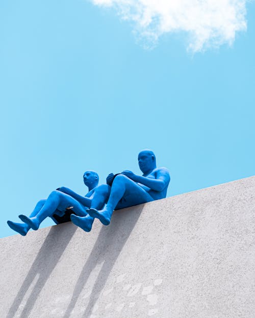 Blue Human Like Sculptures Sitting on a Wall 