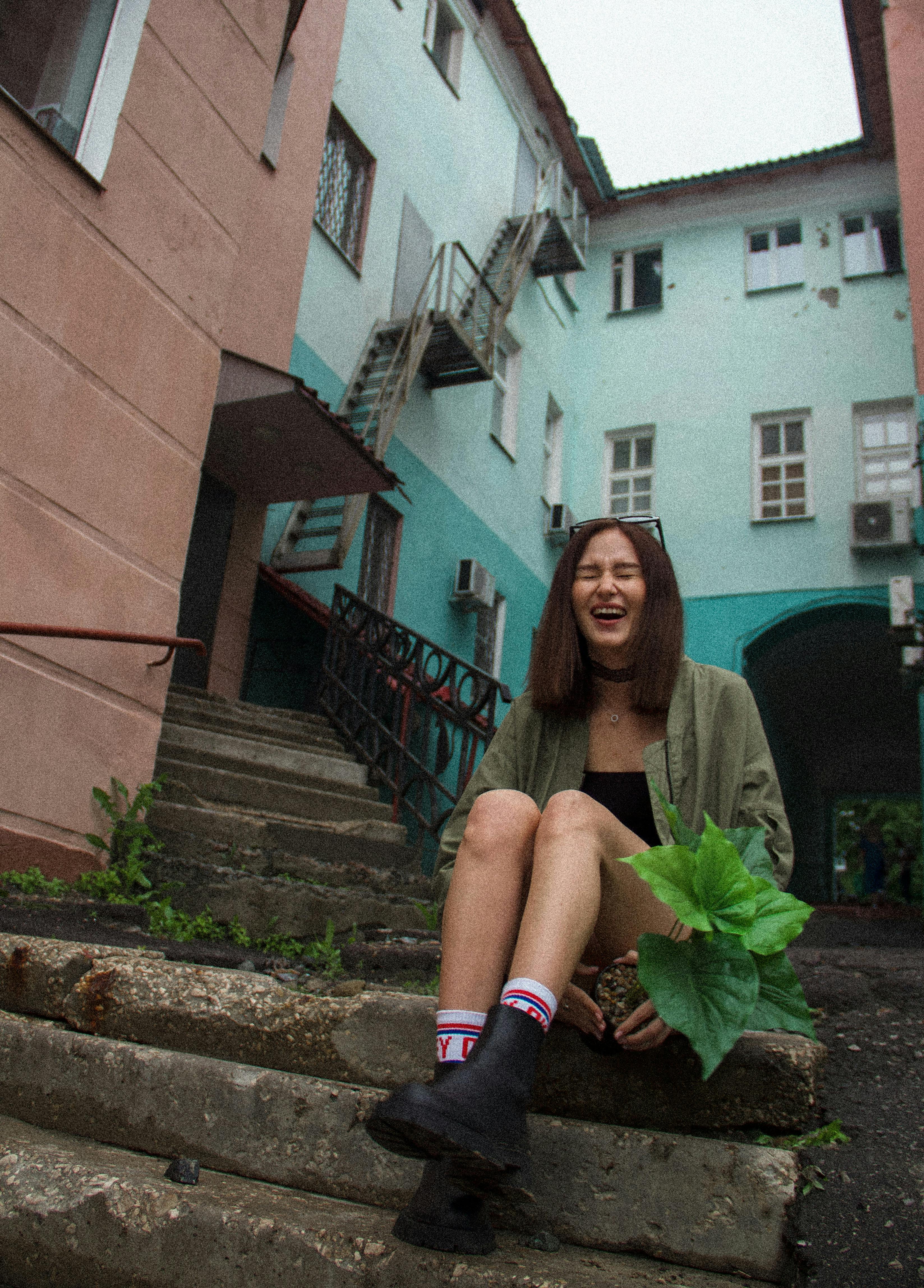 Young woman laughing while sitting on outdoor steps in urban setting.