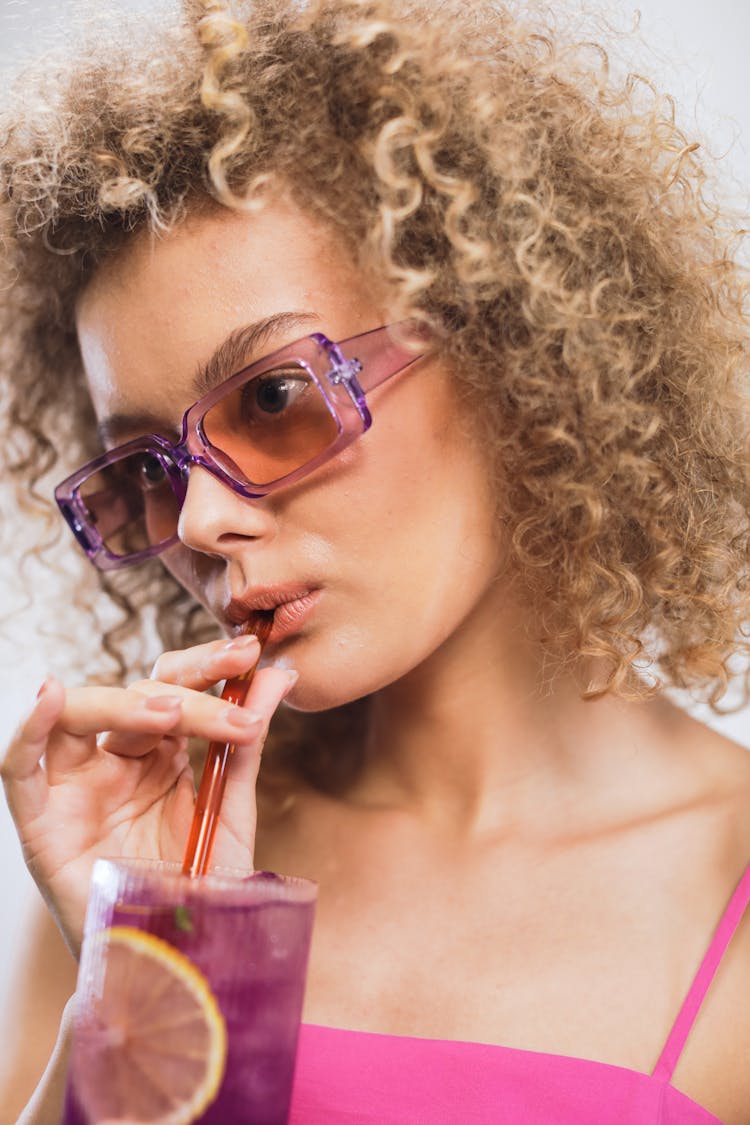 A Woman In Pink Tank Top Drinking Cocktail While Wearing Sunglasses