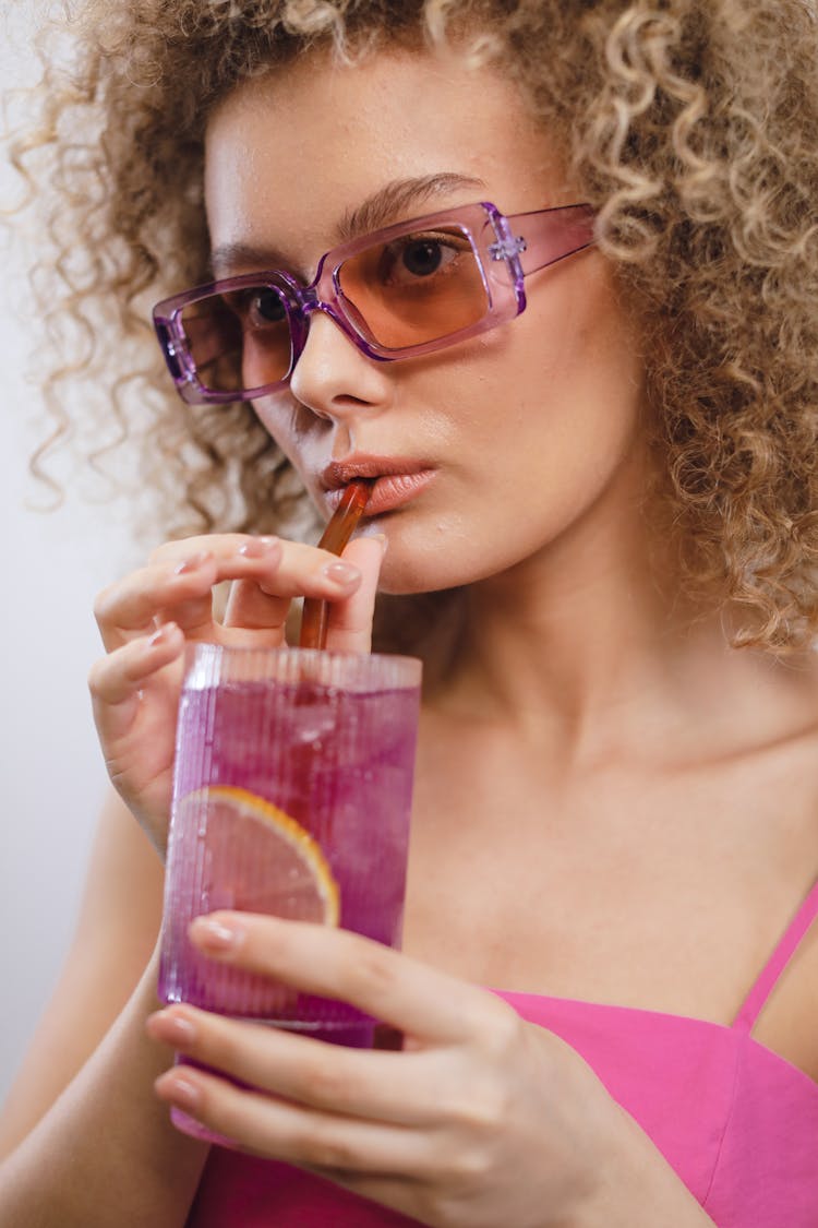 A Woman In Pink Tank Top Drinking Cocktail While Using A Straw