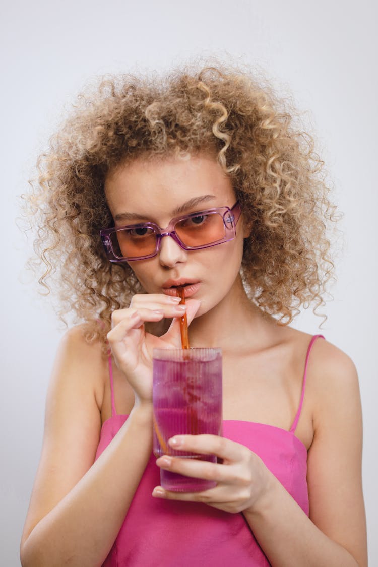 A Woman In Pink Tank Top Wearing Sunglasses While Drinking Cocktail