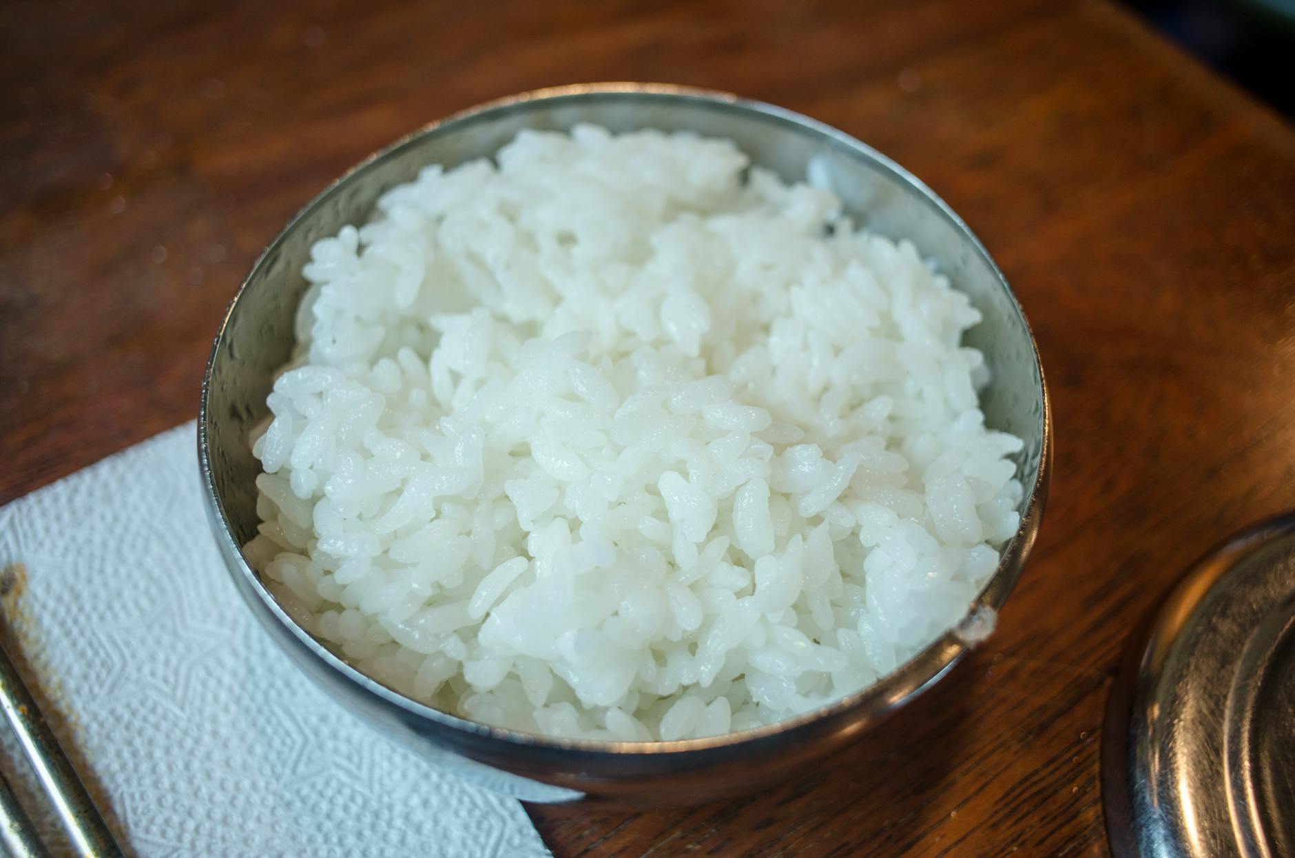 White Rice In A Bowl With Steam Rising, Placed On A Wooden Table At Night