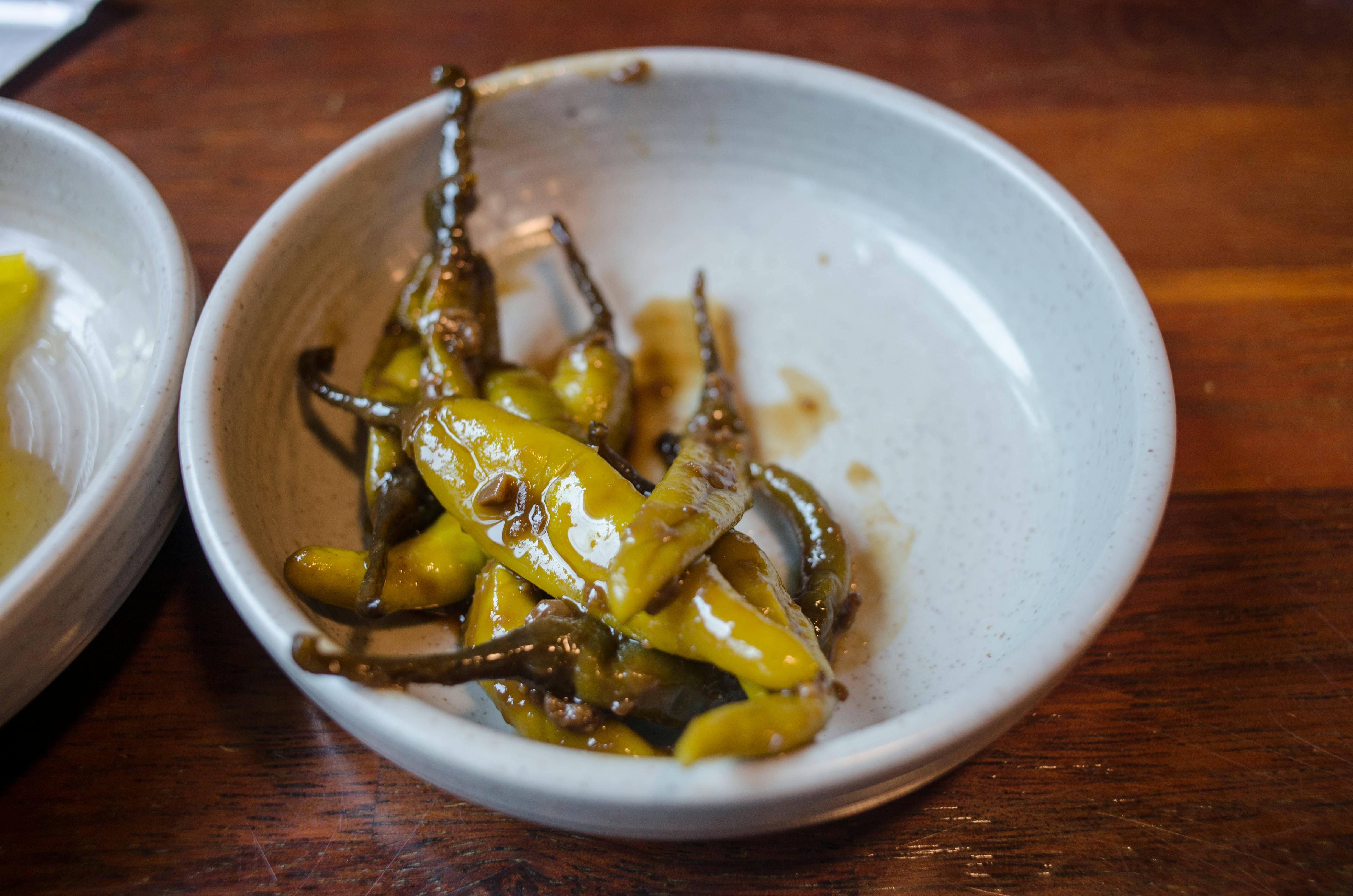 A bowl of marinated green chili peppers on a wooden table surface.