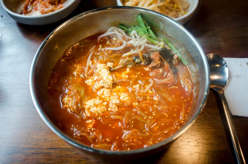 Sundubu jjigae with soft silken tofu and vegetables in a spicy red broth in a stainless steel bowl