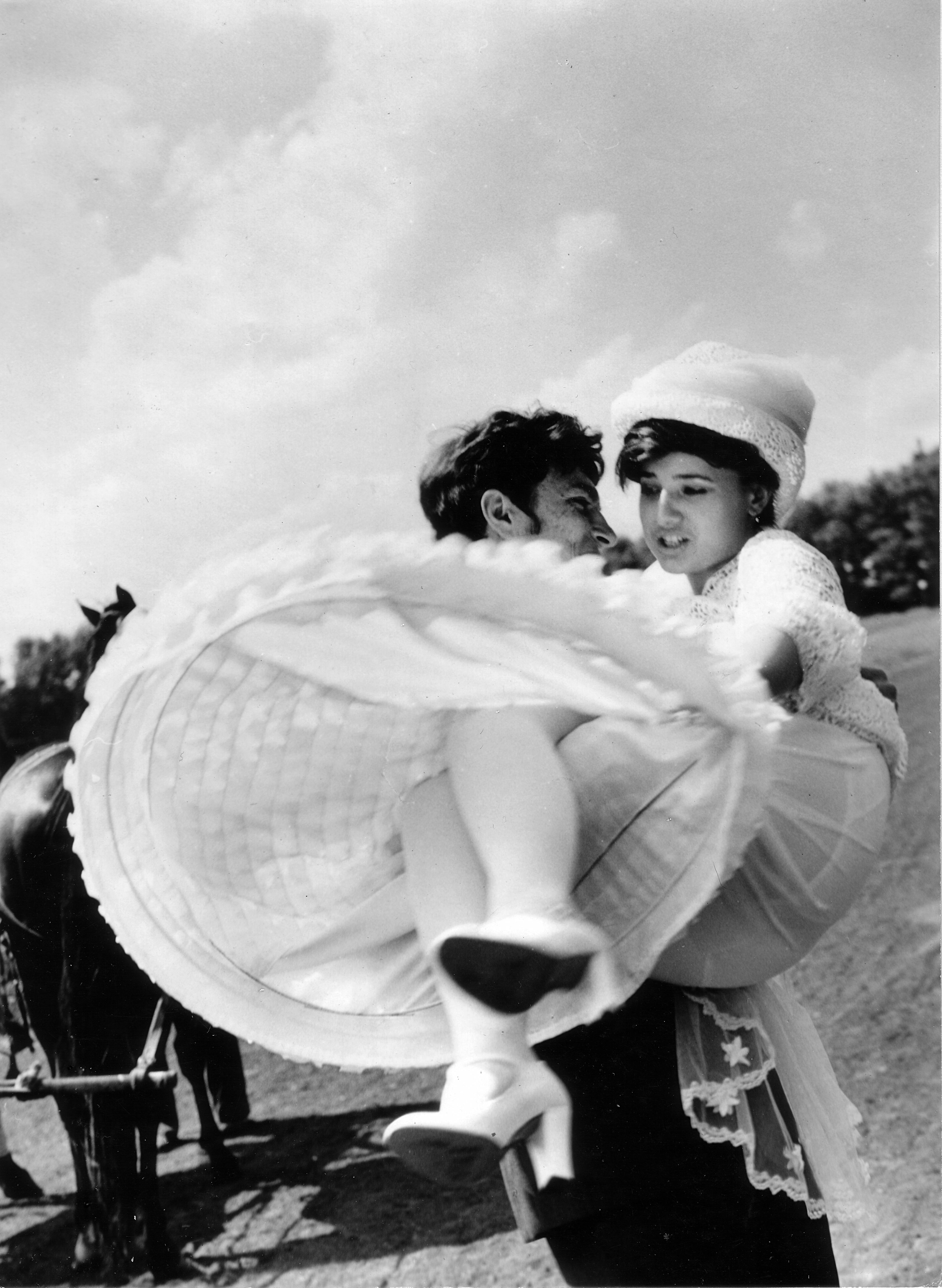 A classic black and white photo of a groom lifting his bride outdoors on their wedding day.