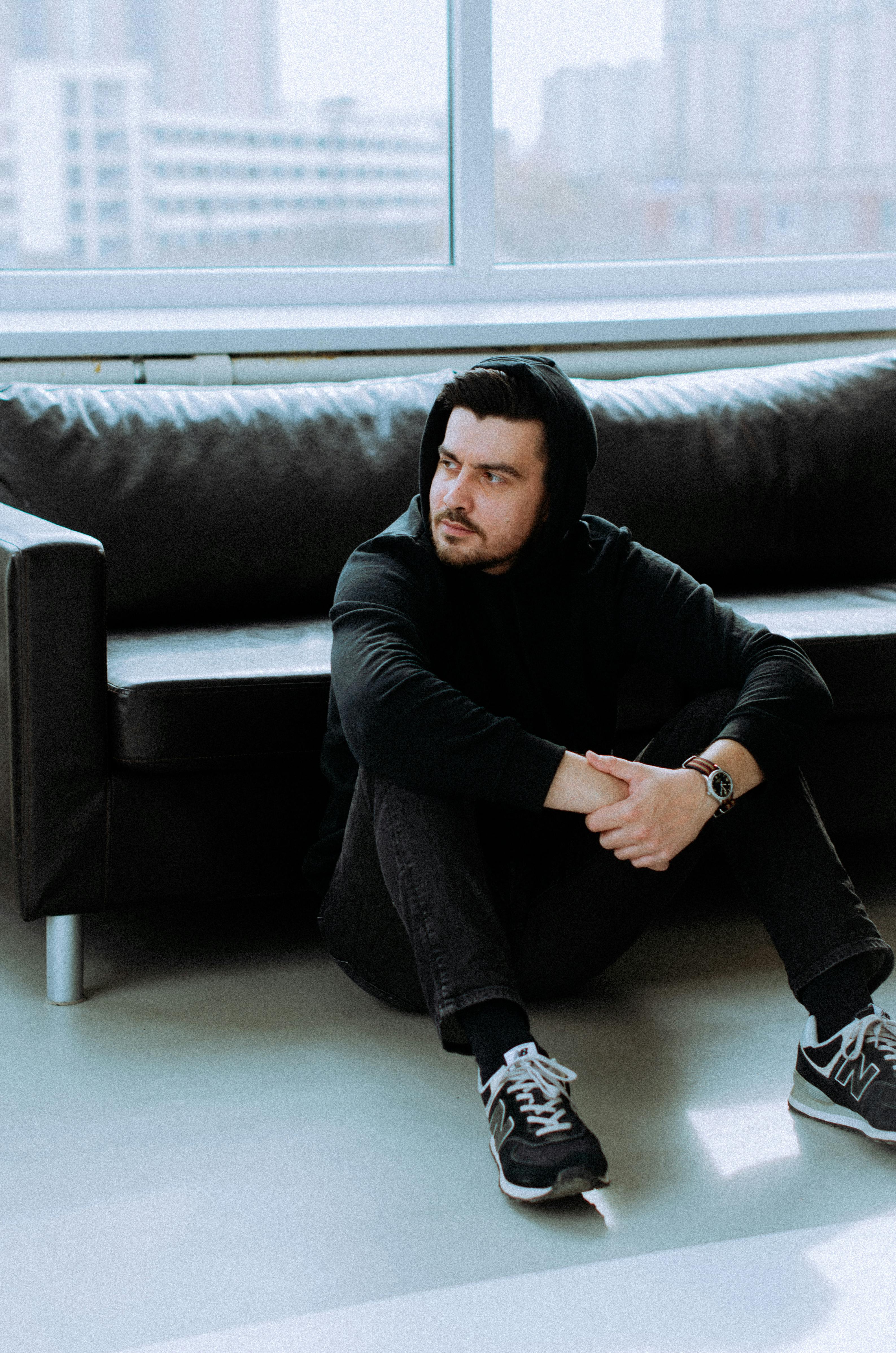 Man in a hoodie sits thoughtfully beside a modern window