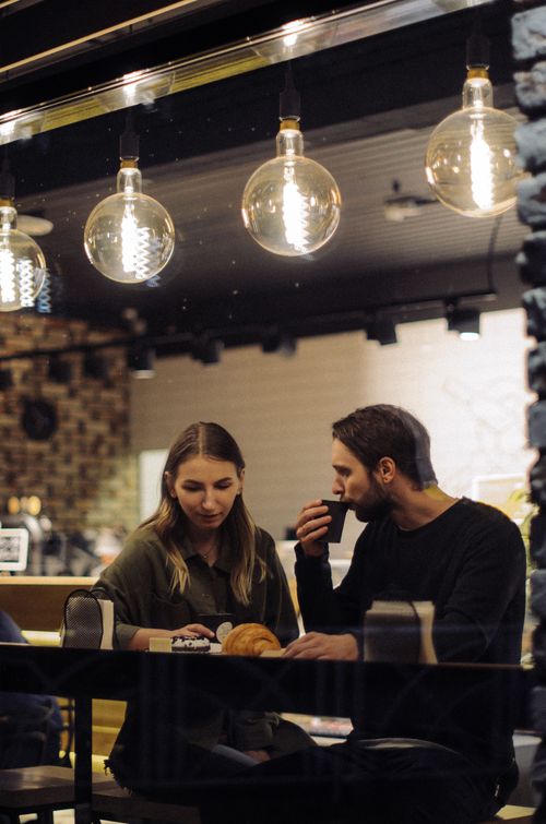 Free Couple enjoying a cozy evening in a trendy café with warm lighting. Stock Photo