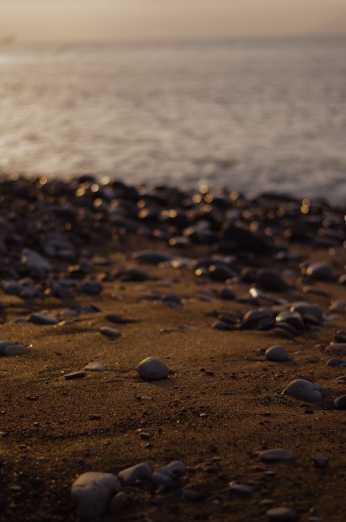 Free A peaceful beach scene at sunset featuring rocks and sand gently meeting the ocean waves. Stock Photo