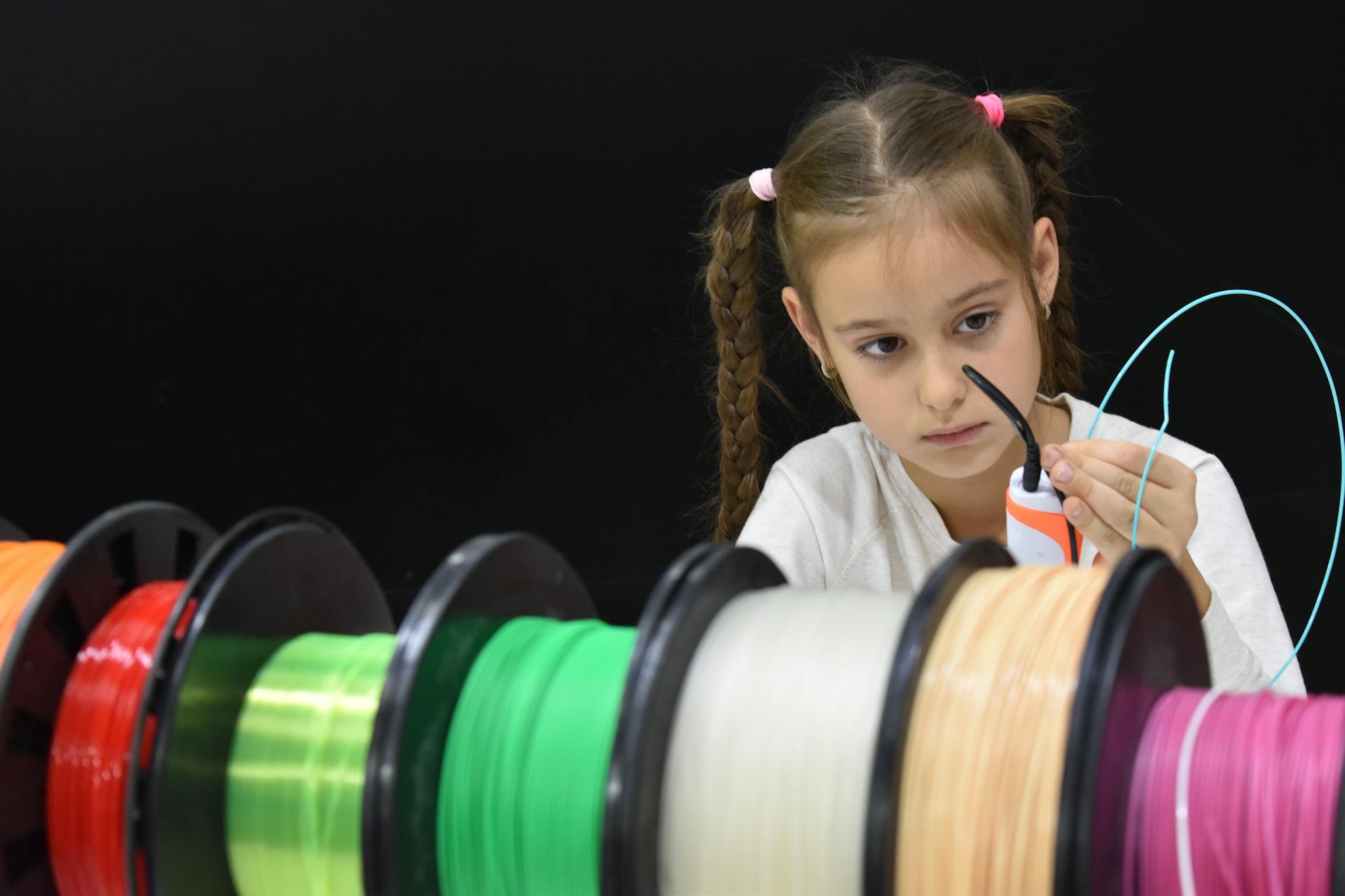 A focused girl with braided hair explores 3D printing using colorful filaments.