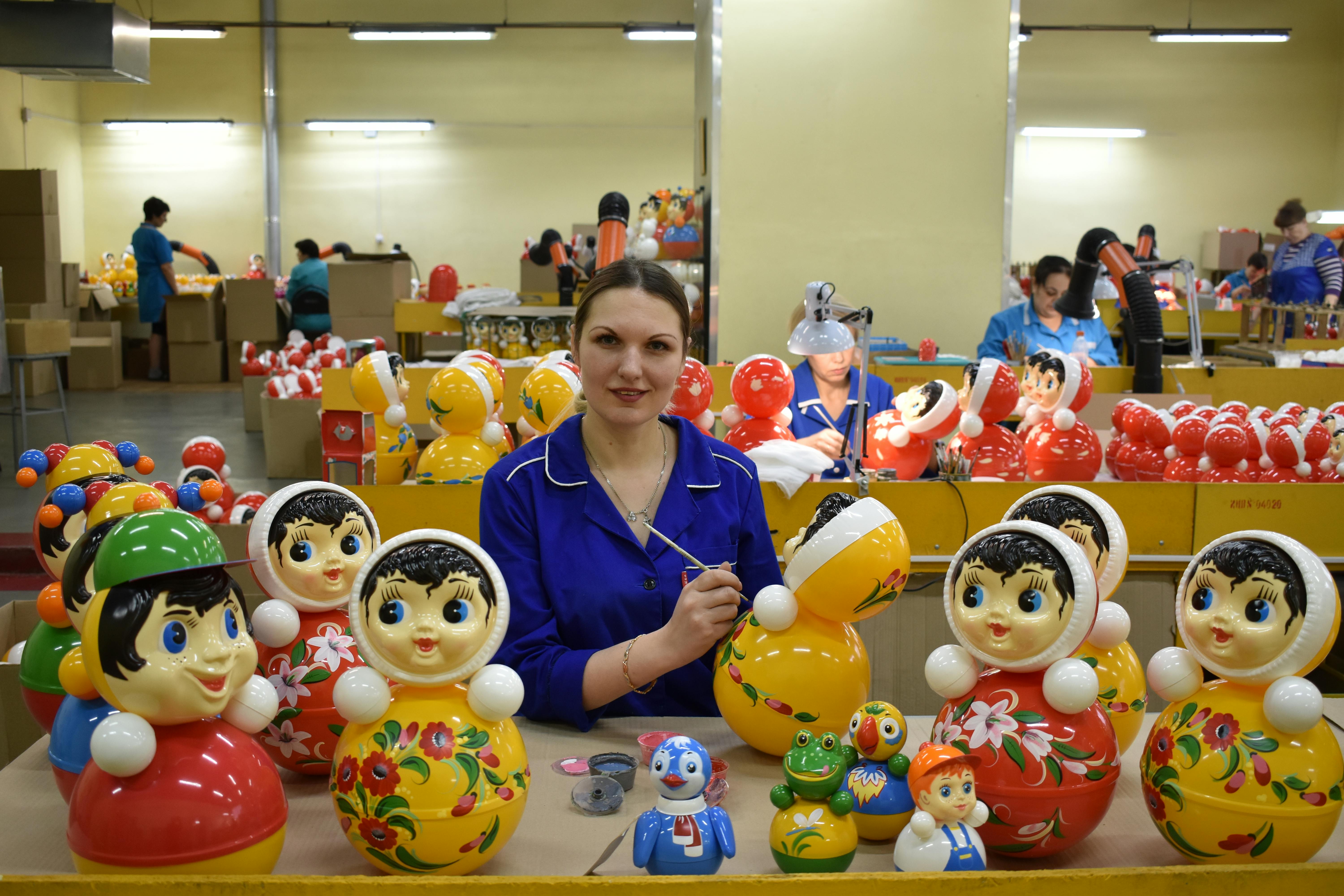 A woman in a toy factory carefully painting traditional colorful toys, surrounded by various dolls.